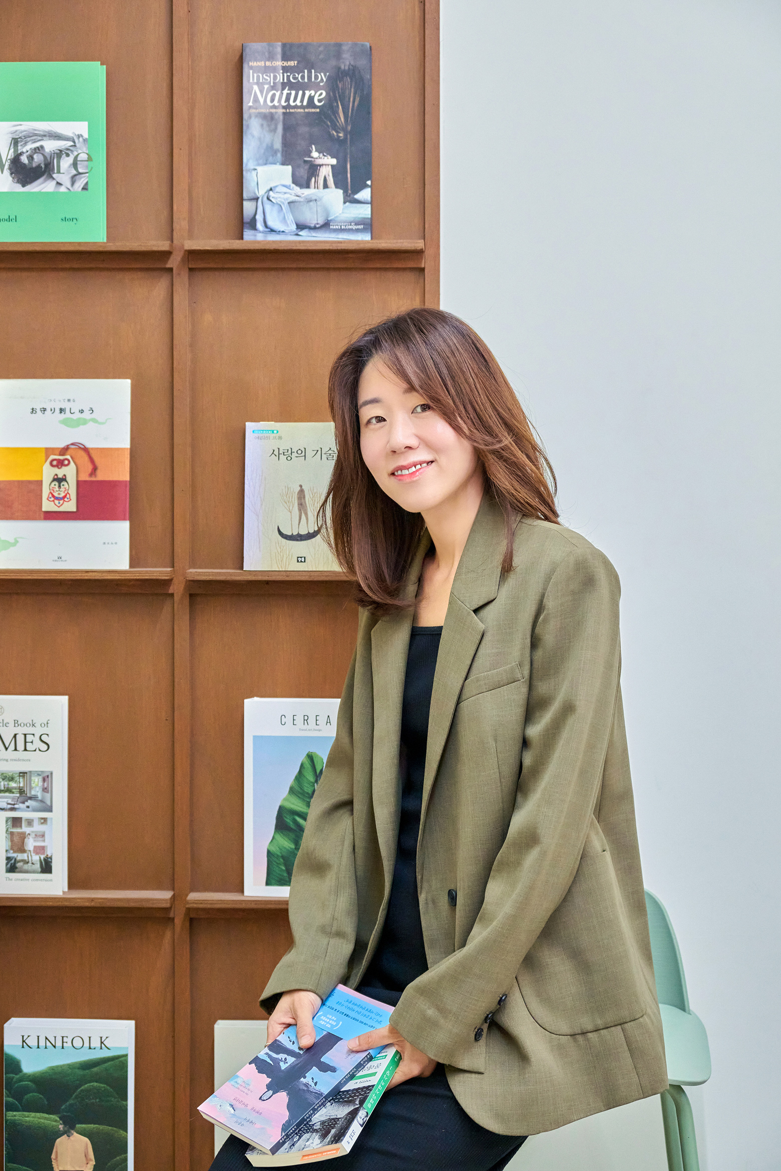 책이 진열된 서가 앞에서 여러 권의 책을 들고 앉아 있는 박지아 편집자